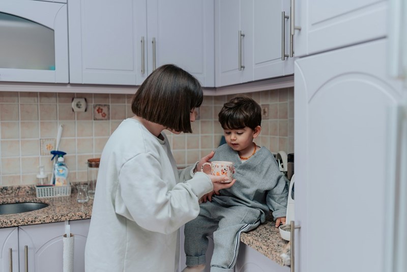 Nanny taking care of a family's child, helping him drink from a cup.