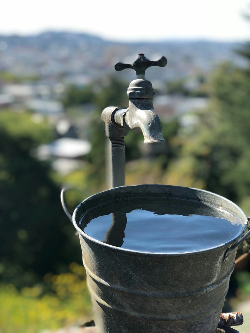 A metal bucket filled with water beneath a faucet
