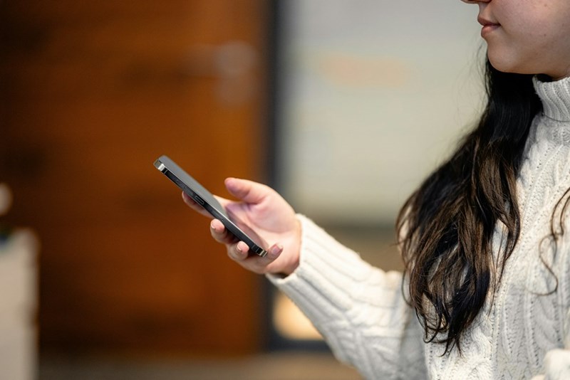 Woman with long brown hair holding a cellphone with one hand.