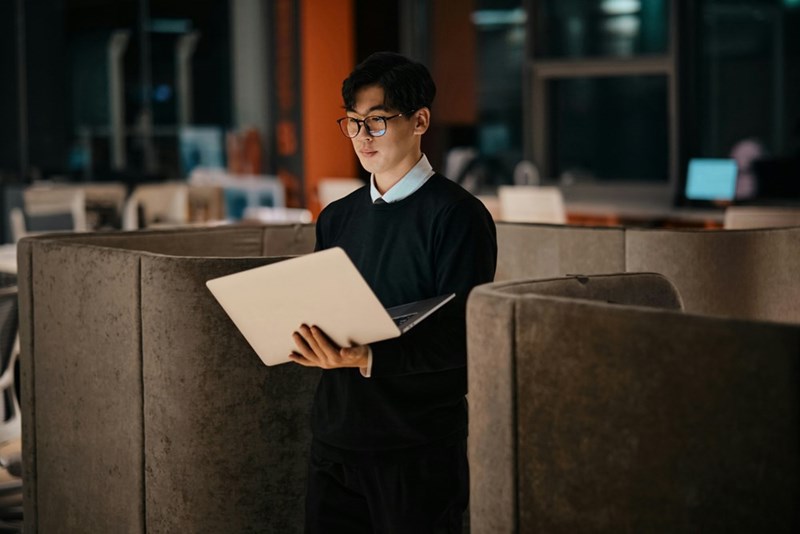 A man holds a laptop in a dark office