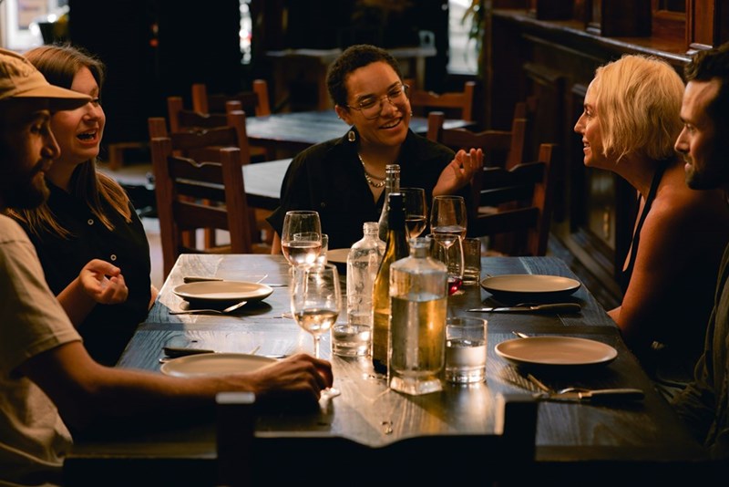 A group of people sit around a restaurant table, talking
