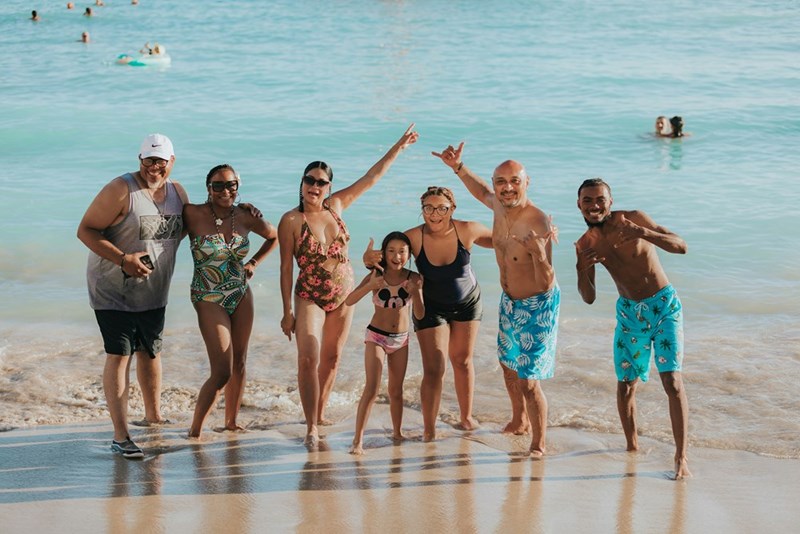 A big family family wearing swimsuits at the beach with cleat turquoise water.