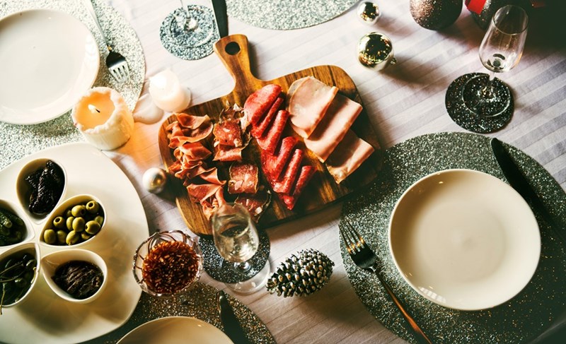 A charcuterie board placed in a well set table with wine, cheese and snacks.