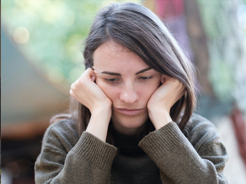 Upset woman with her hands in her hand wearing a grey sweater.