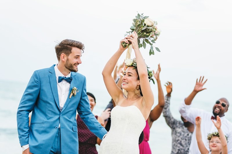 Bride wearing a white dress throwing a bouquet of flowers at her wedding with husband by her side.