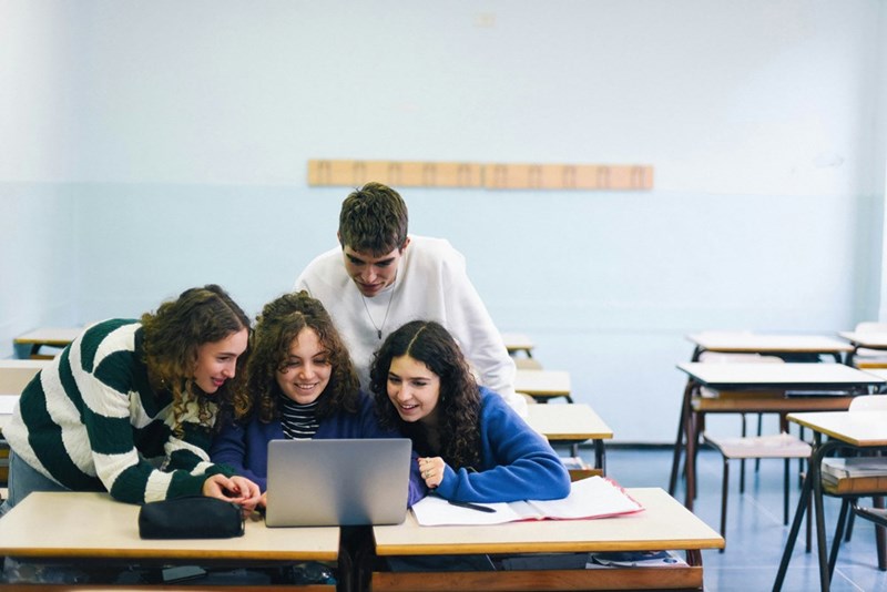 Kids gather together to work on a laptop.