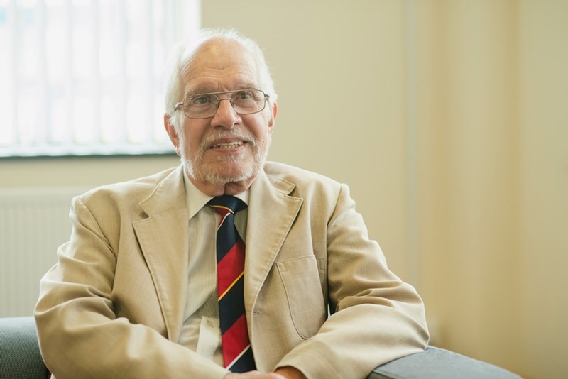 An elderly man smiles in a blazer