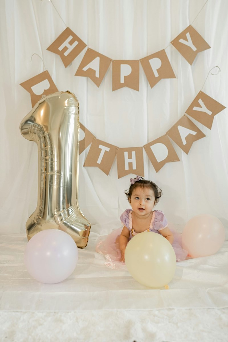 A little girl sitting in front of a number one balloon