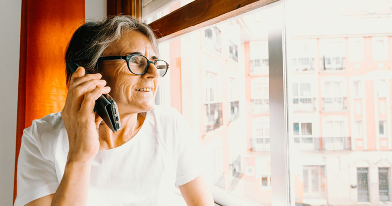 An older woman looks out the window while talking on a cell phone