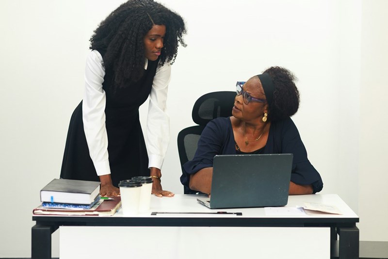 Two women appear to be discussing work at an office desk
