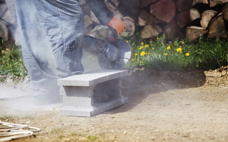 Construction worker generates dust while cutting through a cinder block.