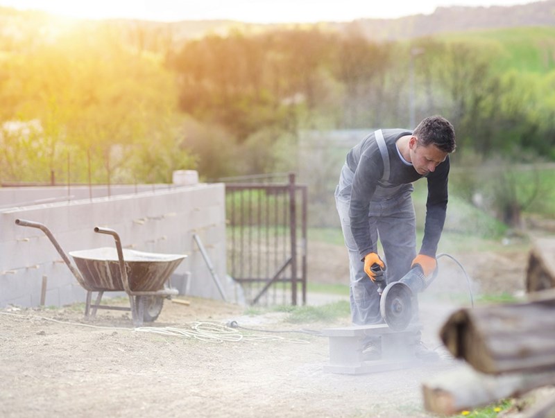 Worker generates cement dust while cutting cinder block.