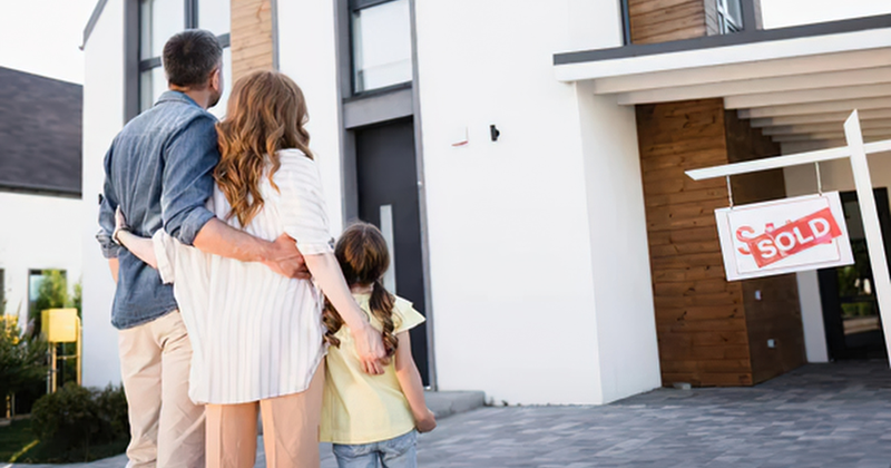 Family looking at their home with sold sign