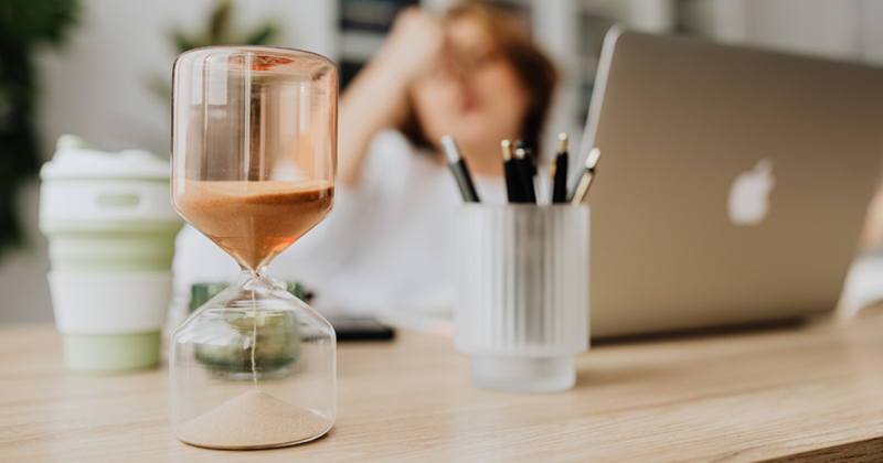 Hourglass on a Desk of a Woman Sitting in front of Her Laptop