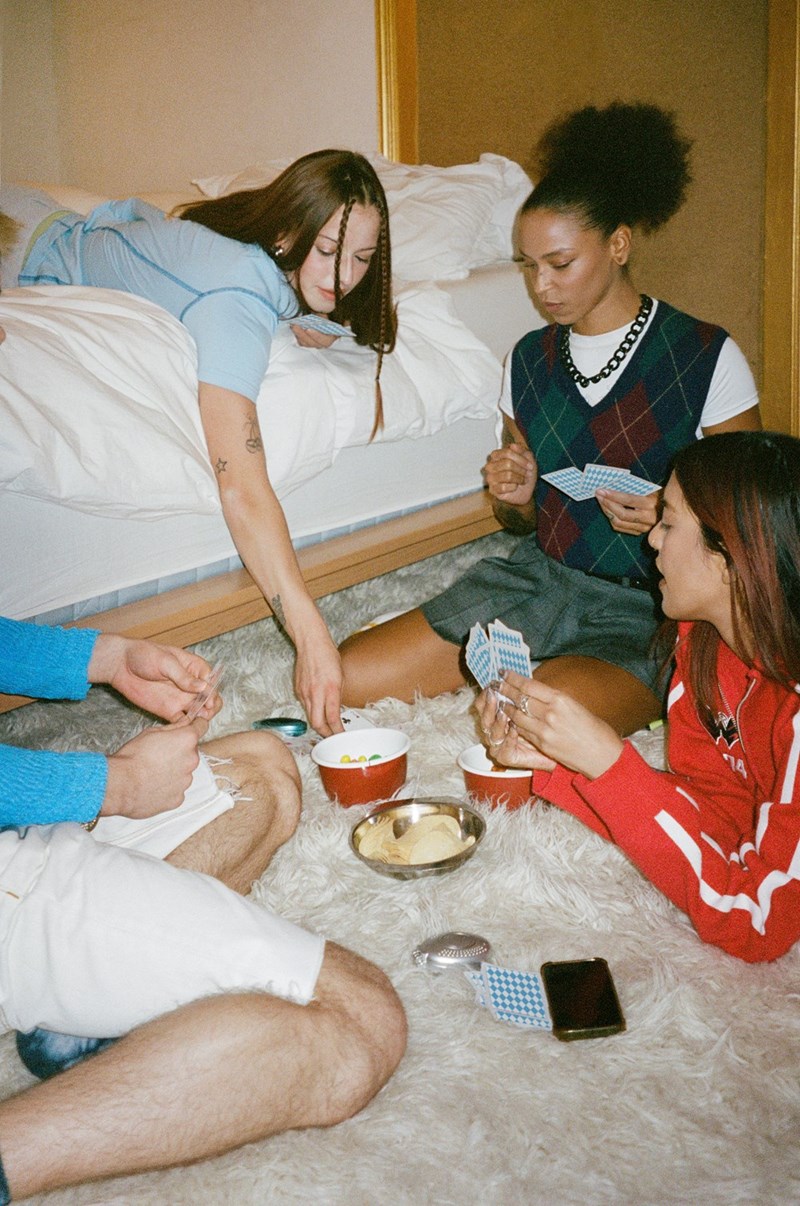 Friends playing cards and eating snacks on the floor during a cozy indoor game night.