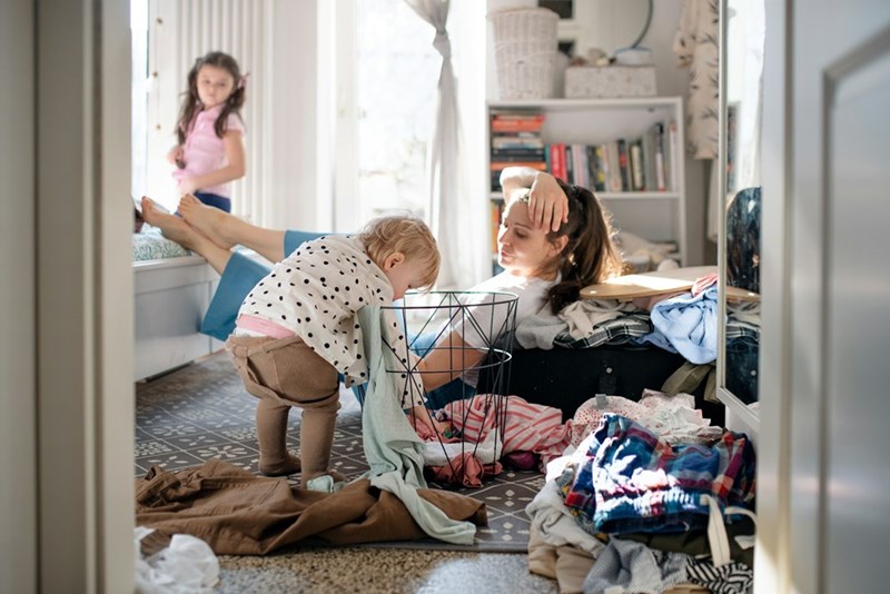 A mom watches as her toddler undoes a pile of freshly folded laundry.