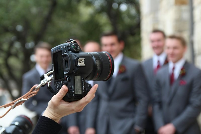 A camera focuses on groomsmen posing together for a formal wedding shot.