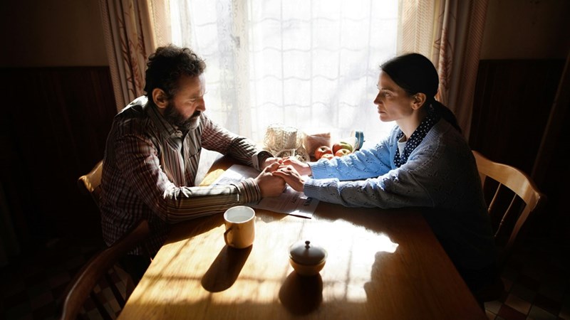 Mand and woman sitting down holding its hands on a wood table with a serious face.