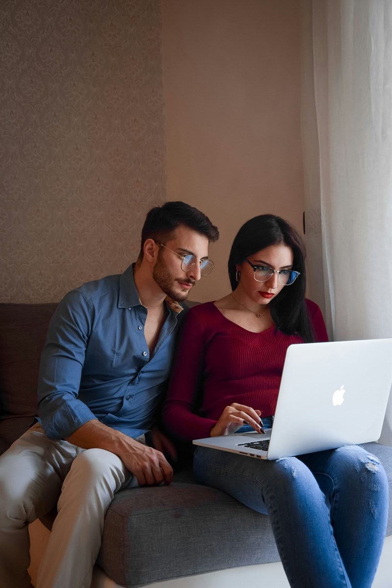 Woman and man sitting on a couch wearing glasses and looking at a computer.