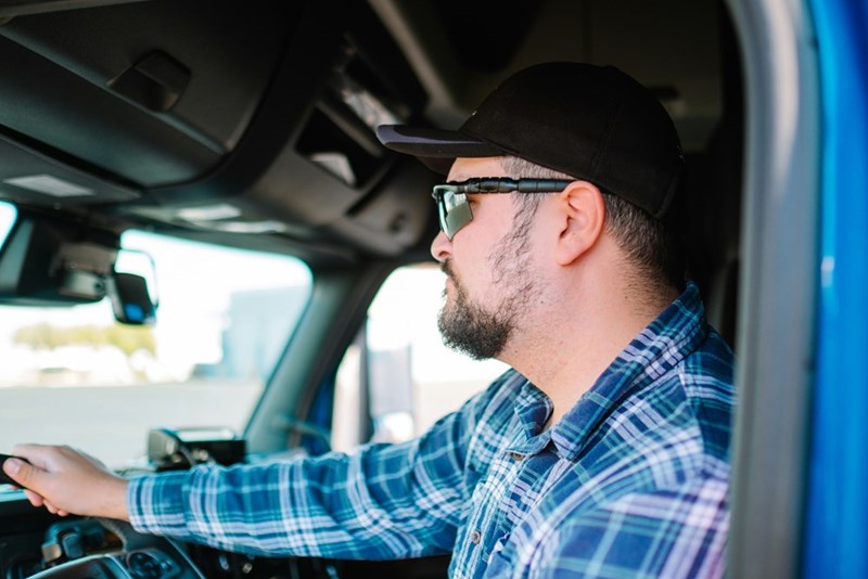 A man wearing sunglasses and a flannel shirt drives his truck.