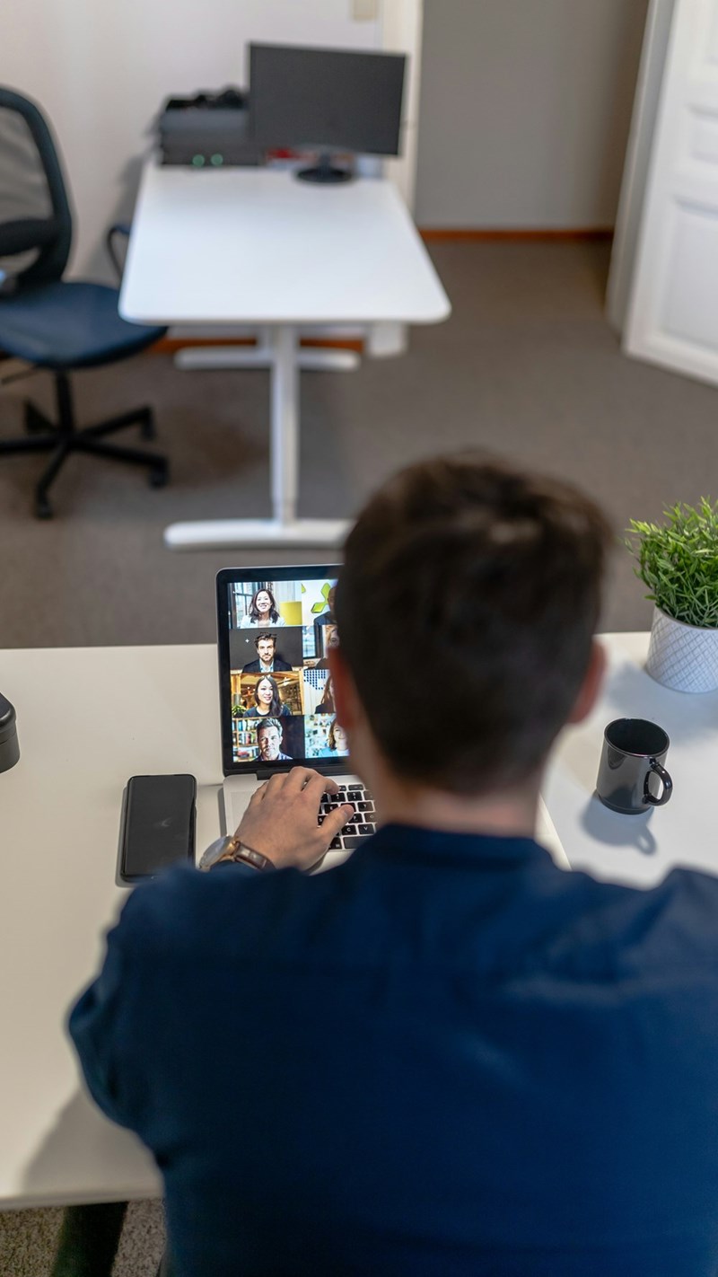 Man working on laptop during group video conference call at home office desk.