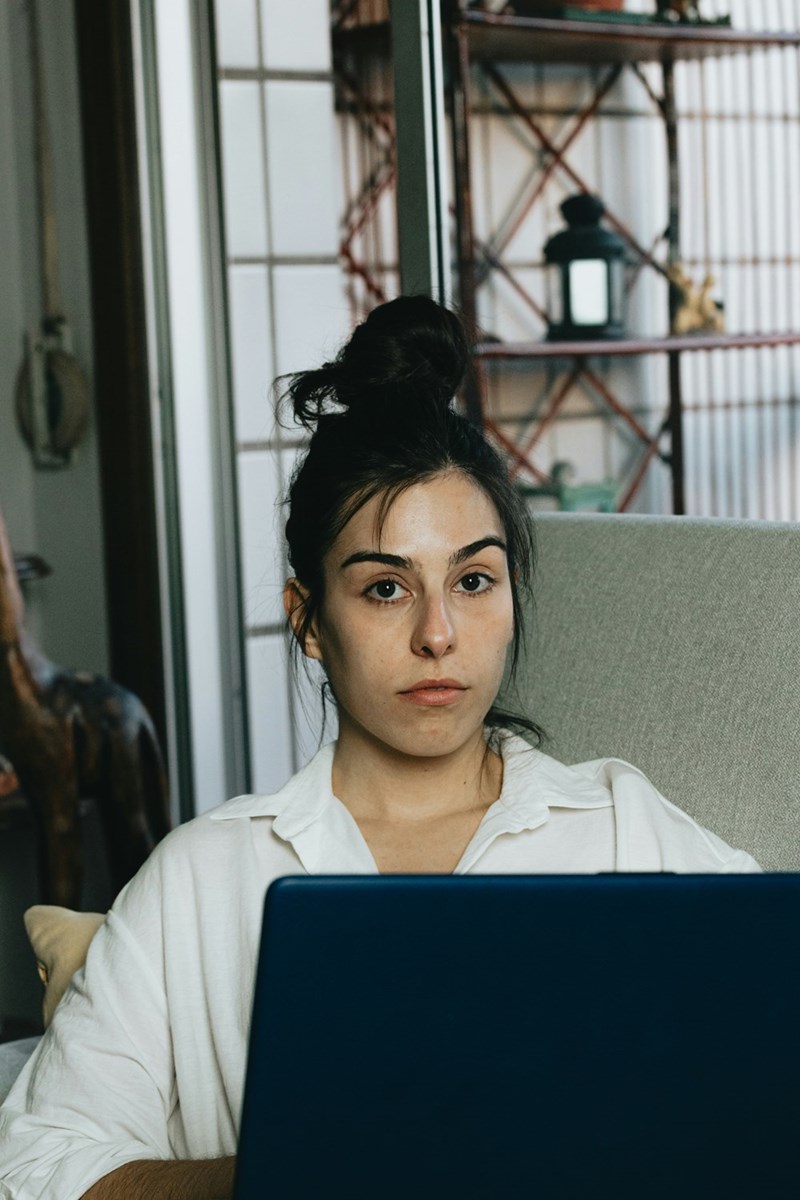 Woman using laptop at home with focused, serious expression while sitting on couch.