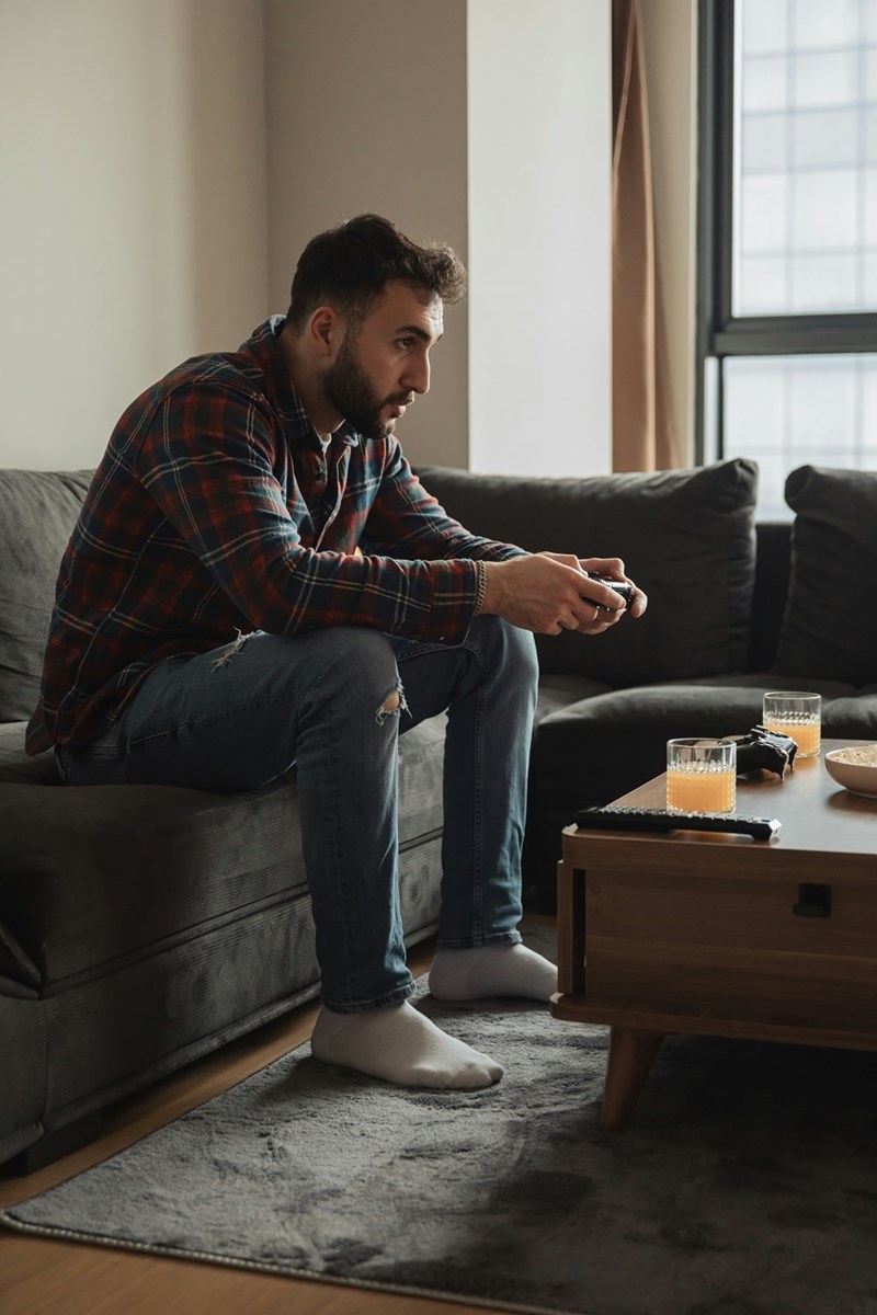 Man playing video games on couch with controller, focused in living room at home.