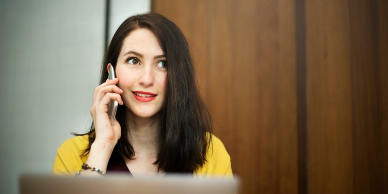 Woman smiling and talking on smartphone indoors, looking to the side.
