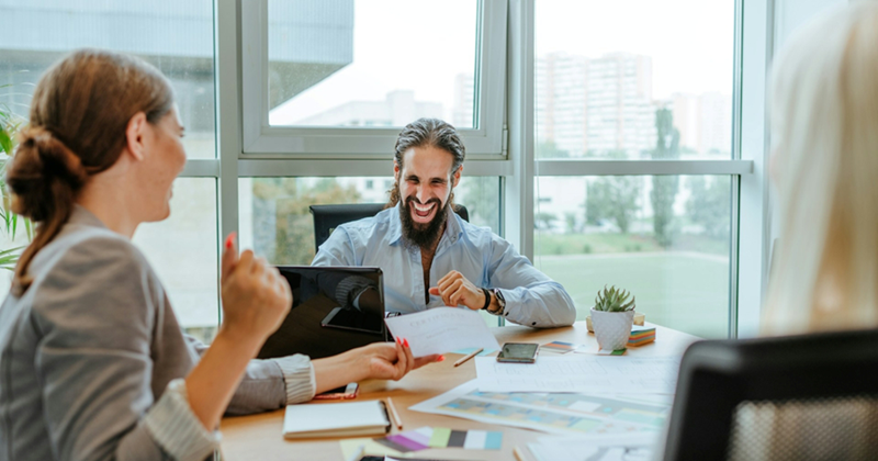 A male employee laughs as a female employee presents a certificate to him across the table