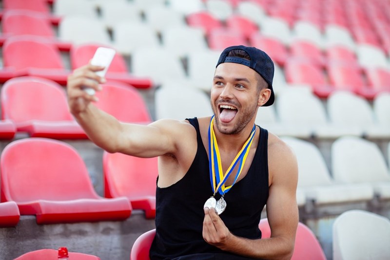 Athlete taking selfie with medals in stadium seating, smiling and celebrating victory.