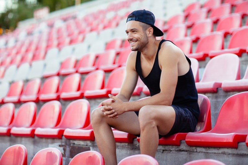 Athlete sitting in stadium stands, smiling and resting after competition.