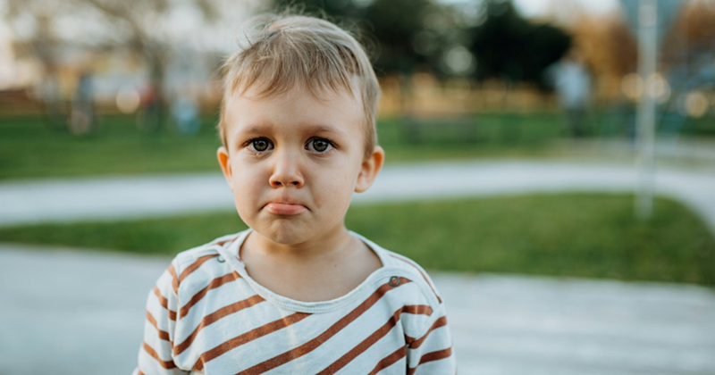 A young boy pouting and crying while stood outside