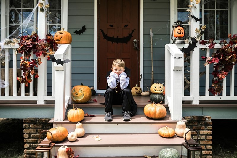 Little boy sits on stairs of house decorated for Halloween with lots of jack o lanterns.