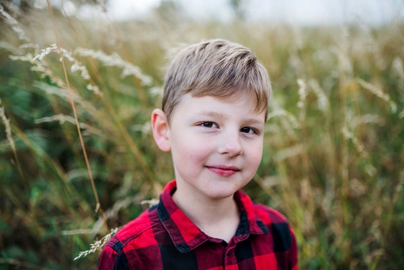 A portrait of blond school boy standing in nature looking at camera