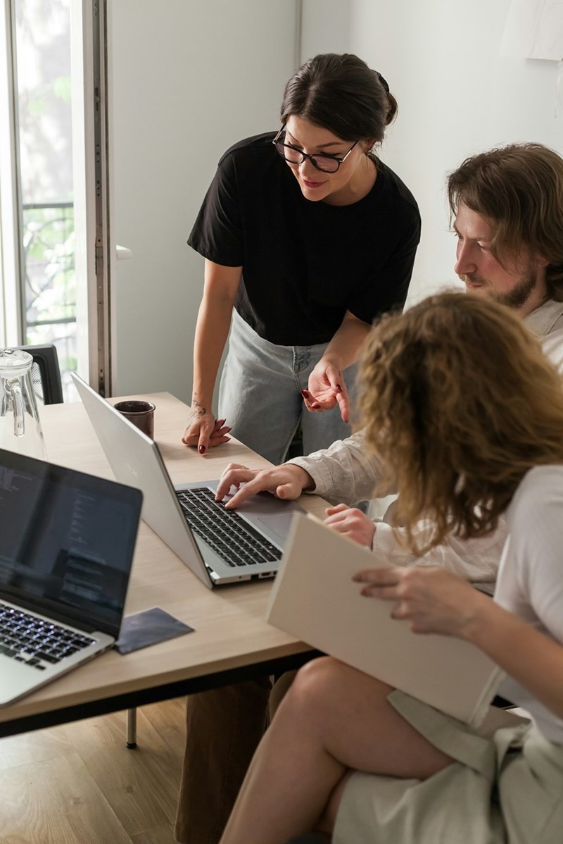 Group of young professionals discussing work in an office by a computer desk.