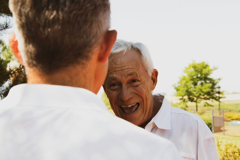 An old grandfather wears a white button-up shirt and smiles during the daytime.