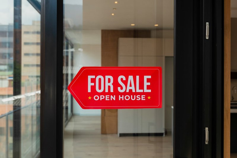 A “For Sale” sign in front of a glass door to a living space.