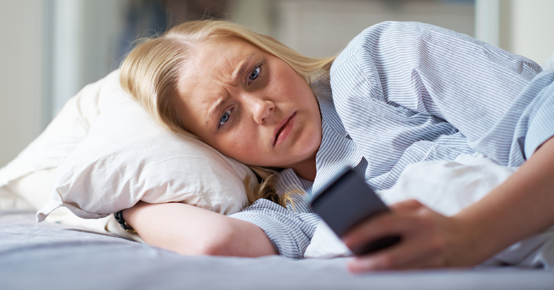 Concerned woman in bed looking at her phone