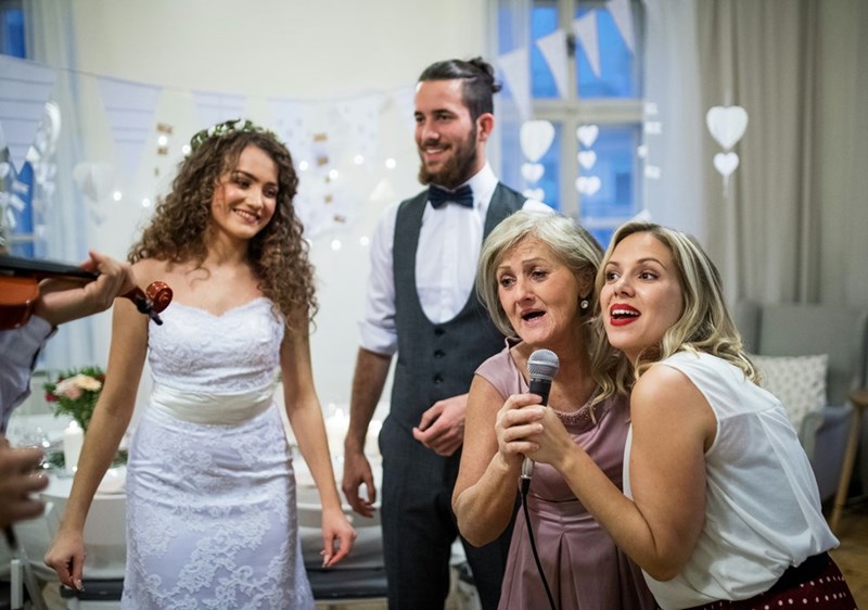 Bride and groom look on awkwardly while guests sing together.