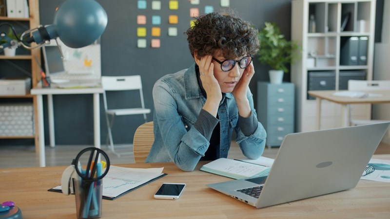 A stressed person sits in front of their laptop in their office