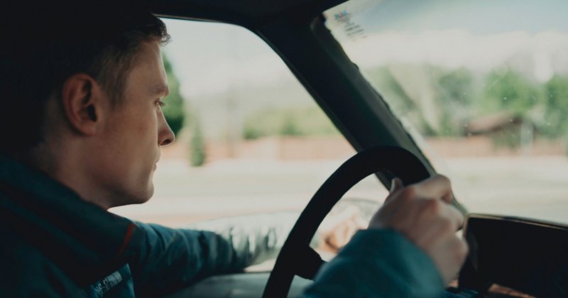 A man drives a car with his arm hanging out the window