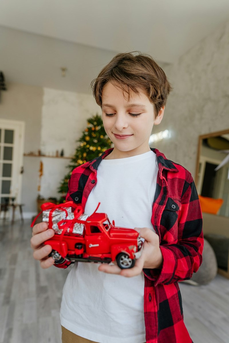 10-year-old boy smiles at a red truck toy in his hands.