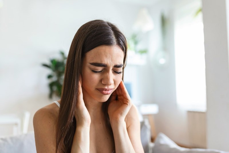 A woman covering her ears in discomfort due to a neighbor's loud music.