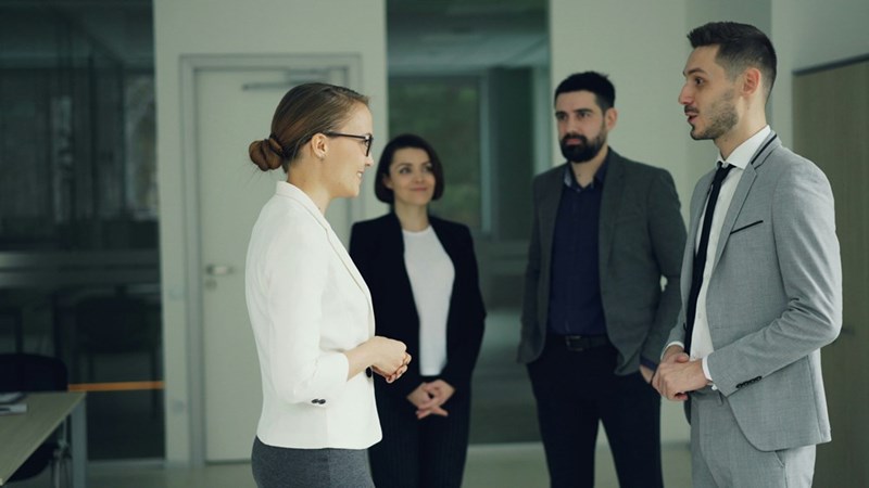 A male and female coworker argue in the office in front of two other employees.