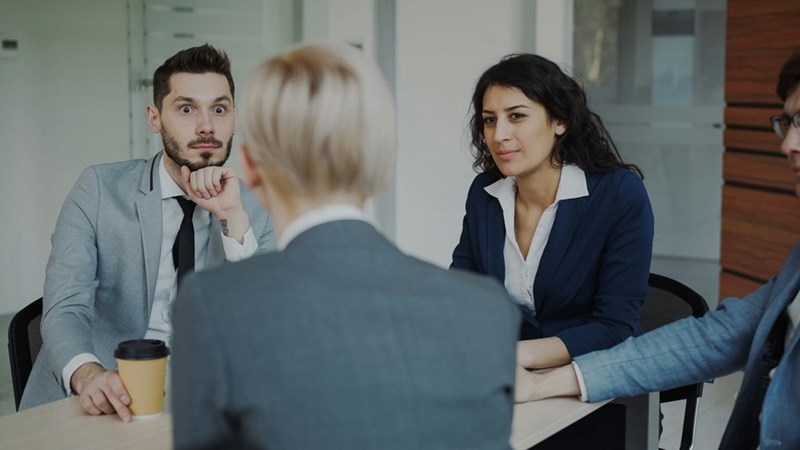 A manager speaks to two employees who look shocked to hear what she has to say.