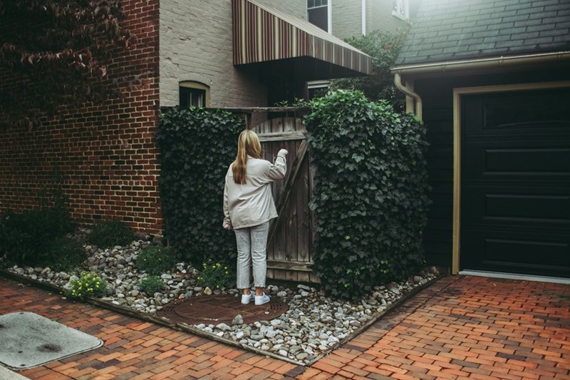 A woman in a brick path knocking a wood door.