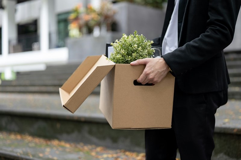 A close-up of a cardboard box of personal items carried by a man in a suit.