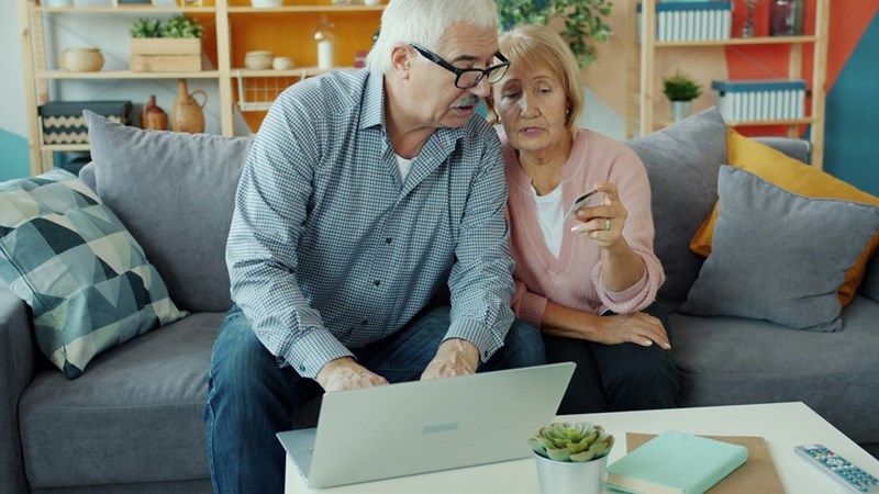 Elderly couple sitting on a couch, looking at a laptop together