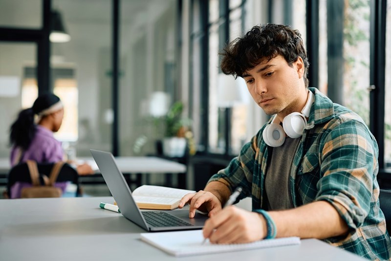 University student writing while using laptop and studying in the classroom