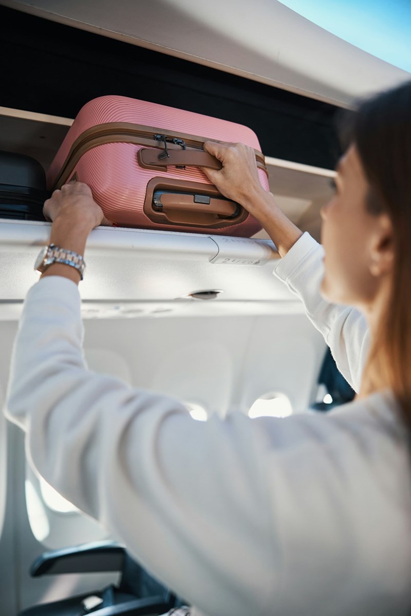 A woman removes her carry-on luggage from the upper compartment of an airplane.